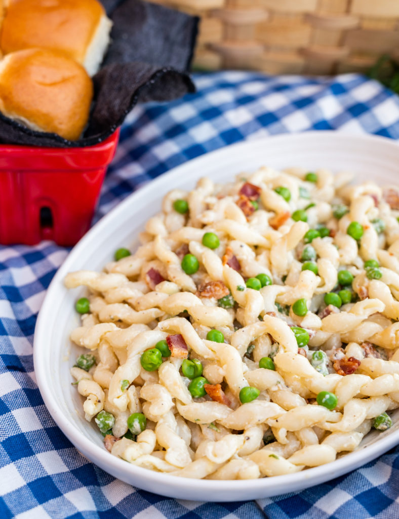 fresh fusilli pasta salad in lemony parmesan dressing with fresh peas and bacon at a picnic